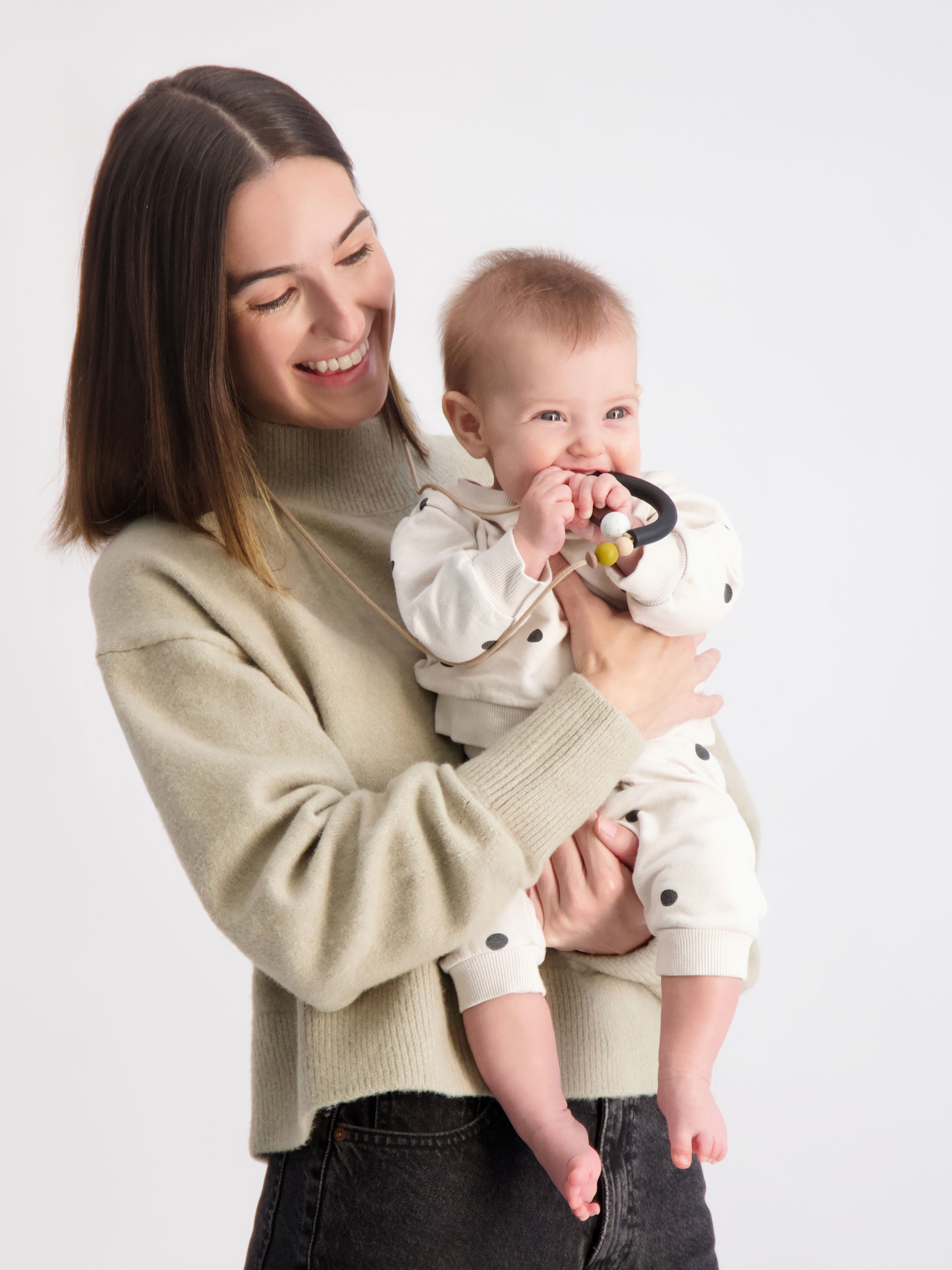 Mom holding her baby as the baby is interacting with our Bloom Teething Necklace in the Liquorice colorway.