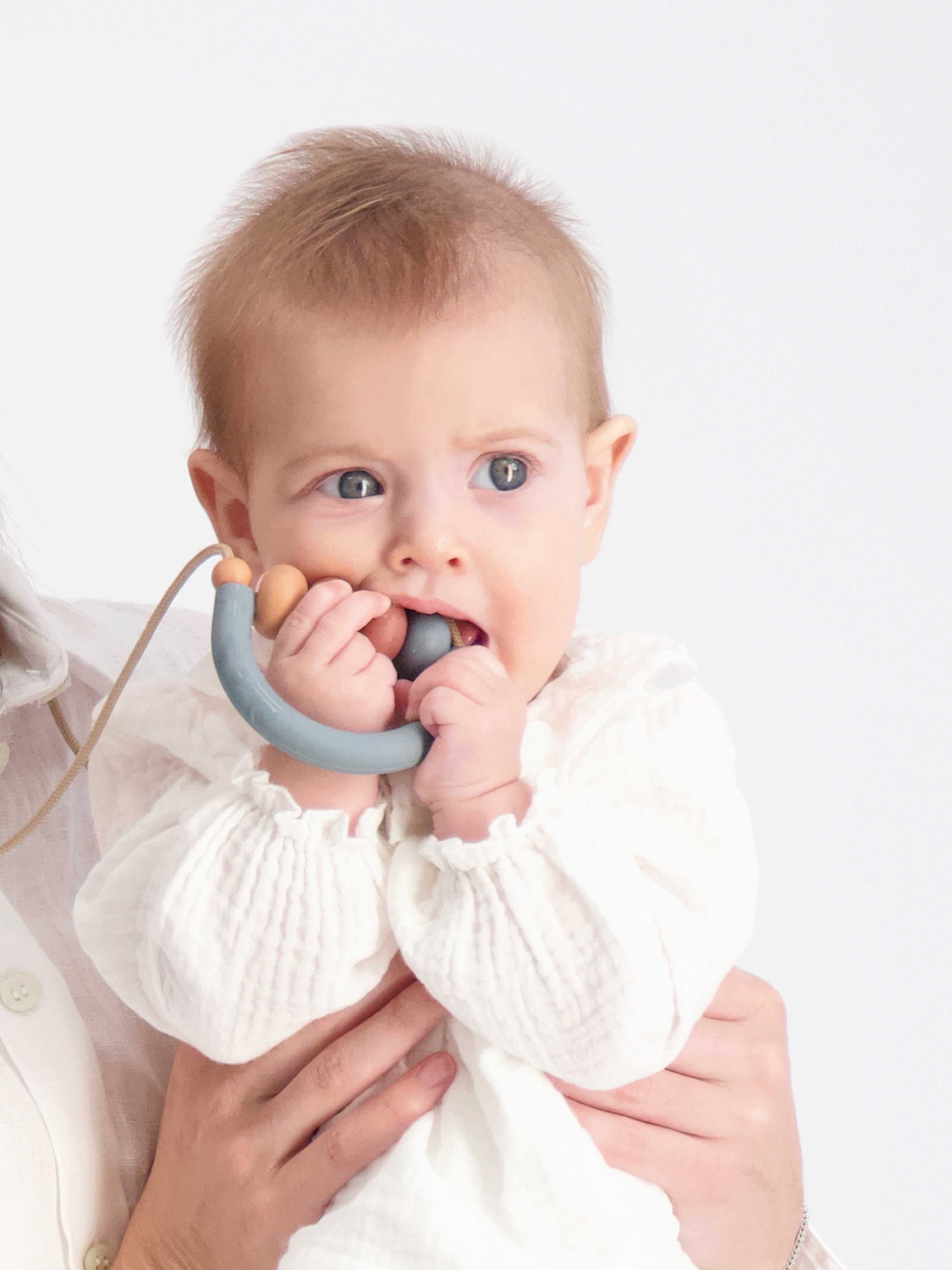 Close-up photo of the baby while mouthing the Bloom Teething Necklace in the Aegean colorway.