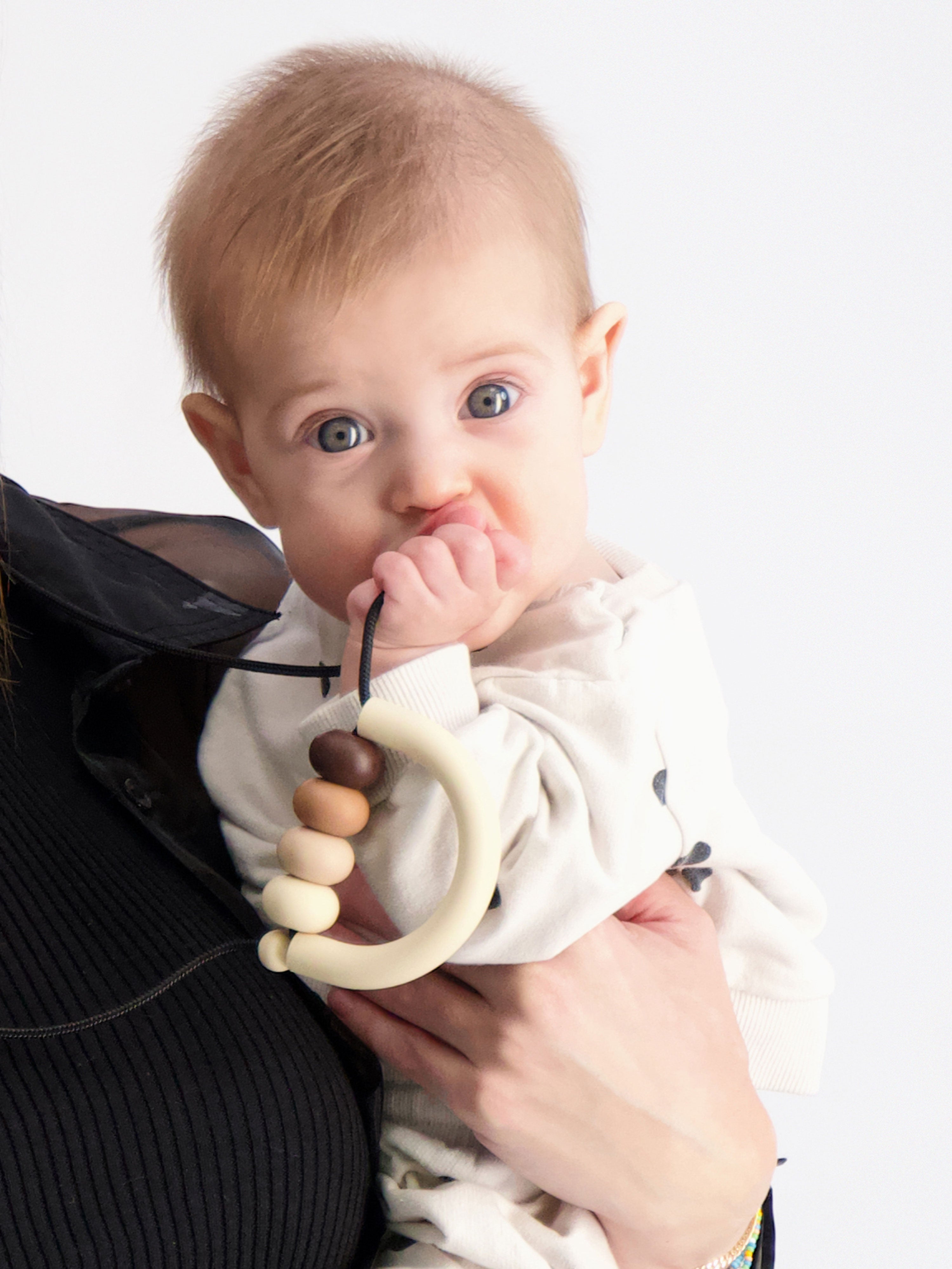 Close-up photo of the baby looking at the camera while holding the Bloom Teething Necklace in the Nutmeg colorway.